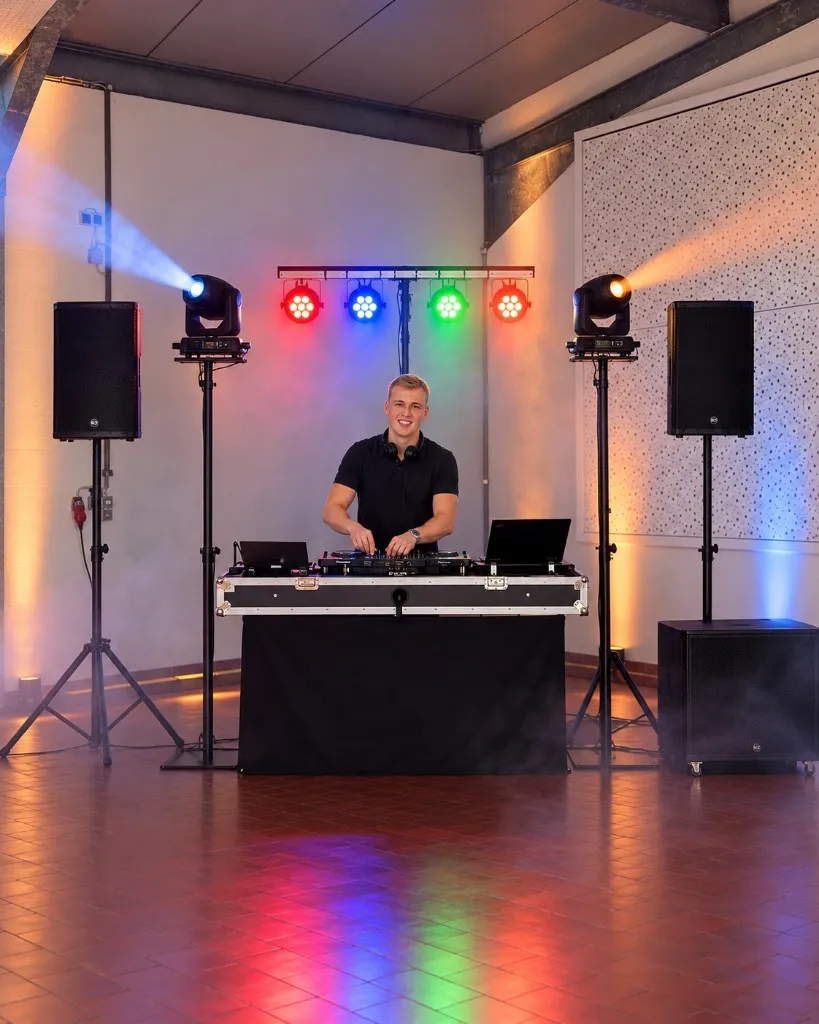 Nick lächelnd am DJ-Pult mit Lautsprechern und Bühnenlicht.